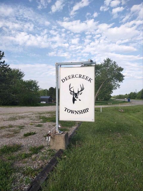 Deercreek Township sign with the township deer logo, posted on a metal frame beside a gravel lot